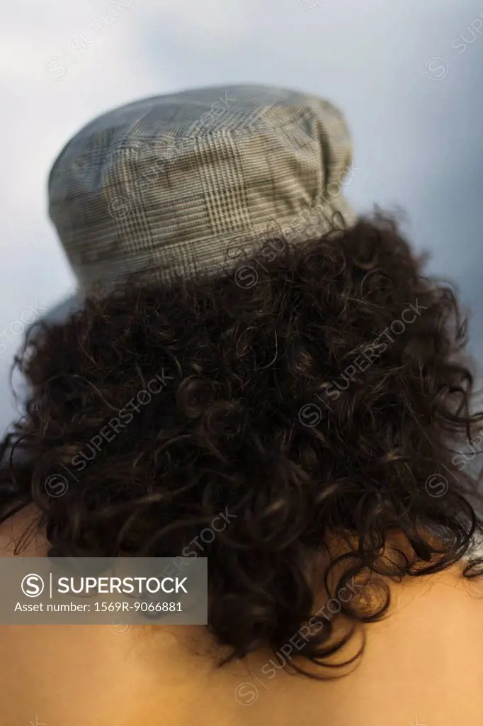 Young woman with curly hair wearing cap, rear view