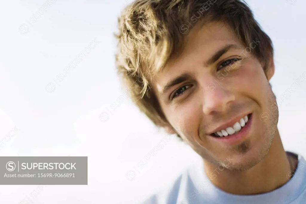 Young man smiling at camera with head tilted, portrait