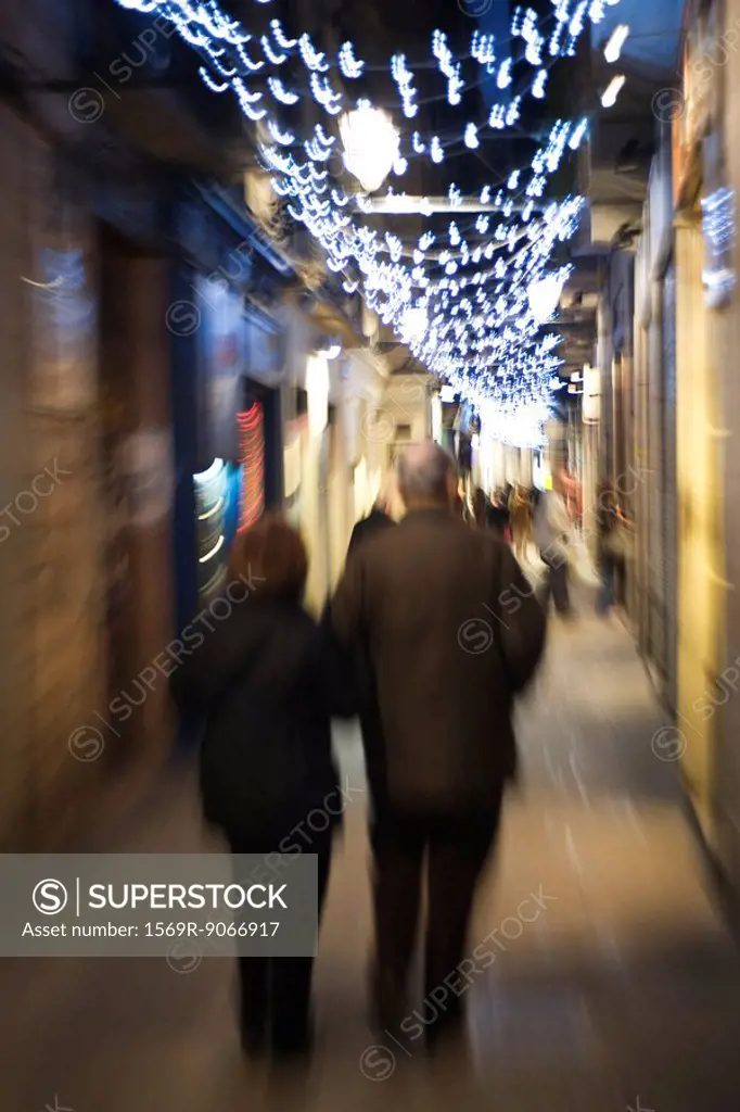Couple walking down alley illuminated by Christmas lights at night