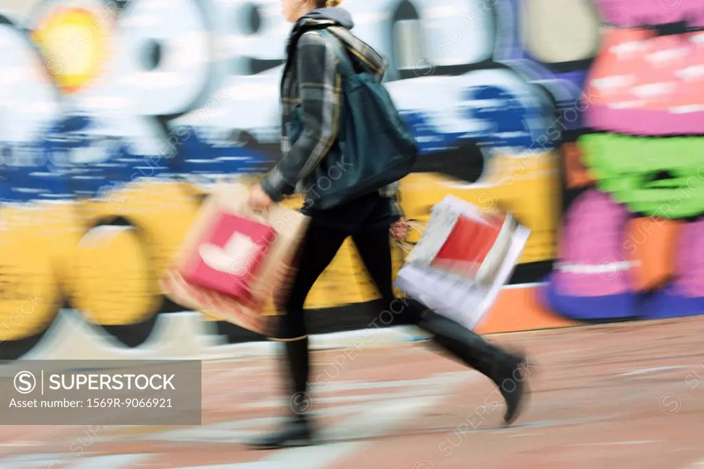 Pedestrian carrying shopping bags on sidewalk, blurred