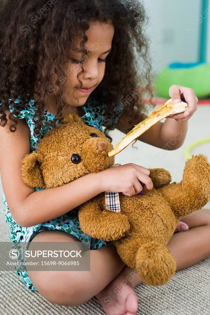 Little girl feeding teddy bear pizza