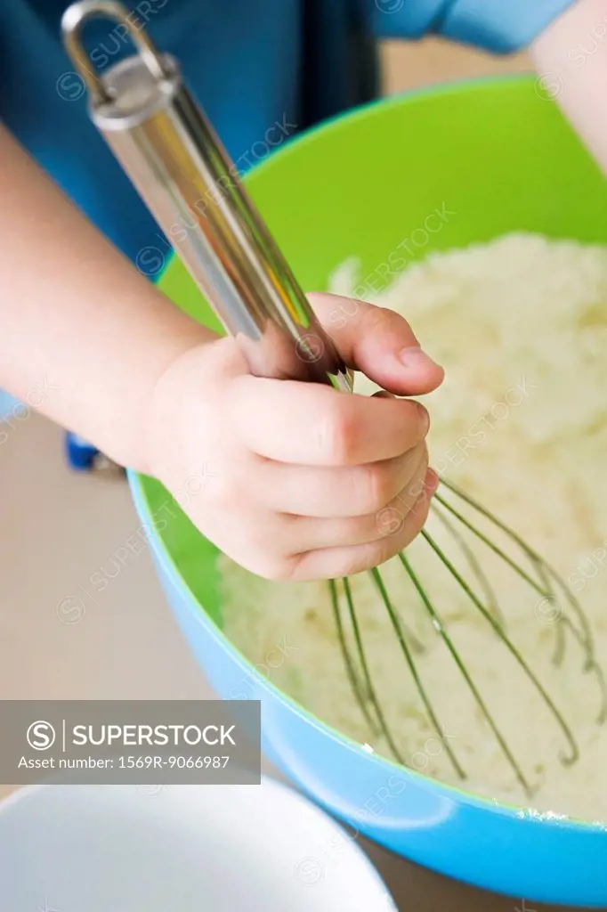 Child stirring batter with whisk, cropped view