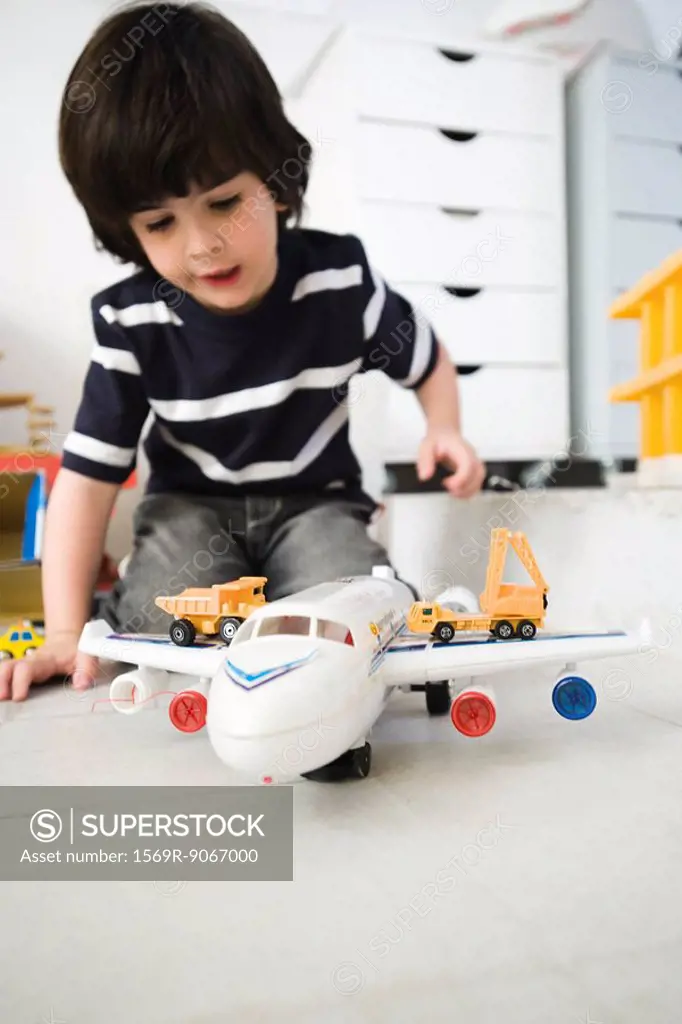 Little boy playing with toy airplane and toy trucks