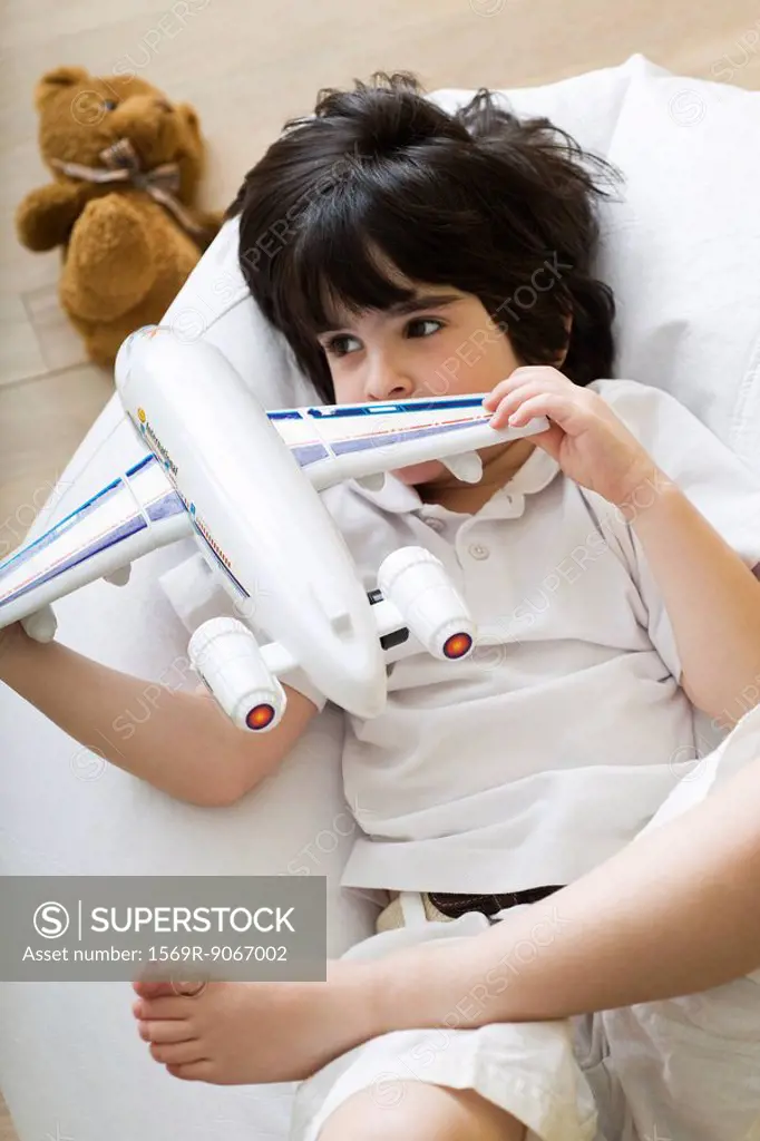 Little boy lying on beanbag chair, playing with toy airplane