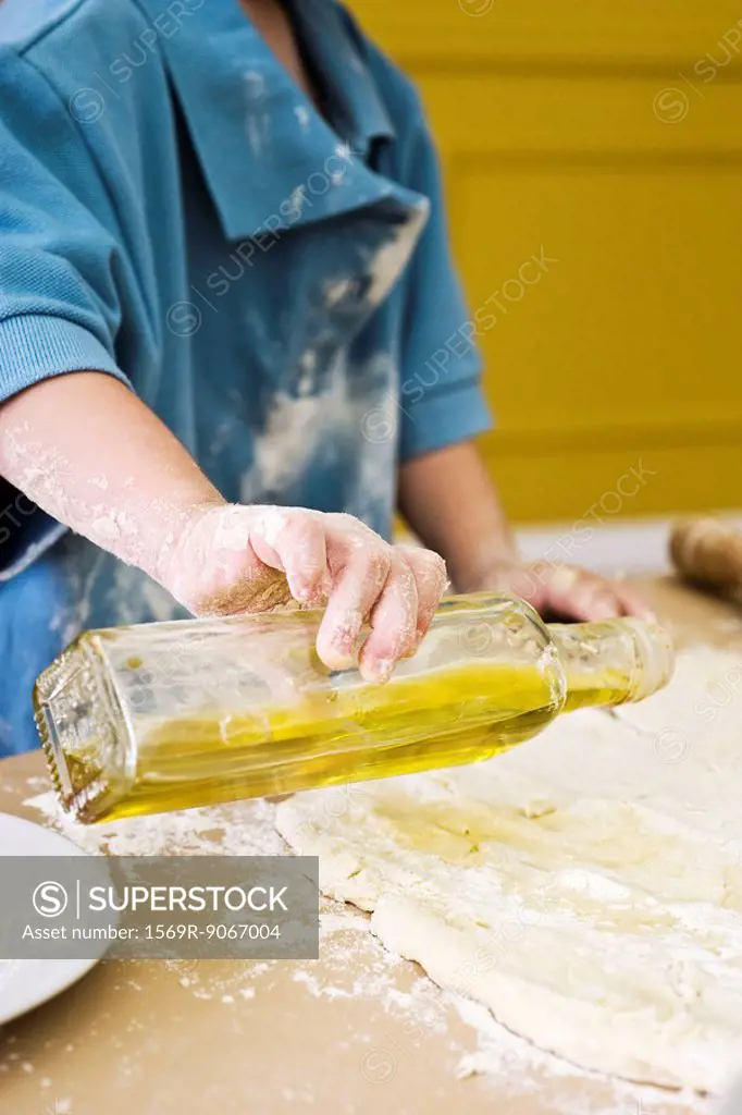 Child pouring olive oil on rolled out dough, cropped