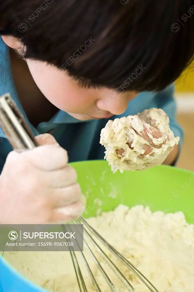 Little boy leaning over mixing bowl, smelling handful of dough