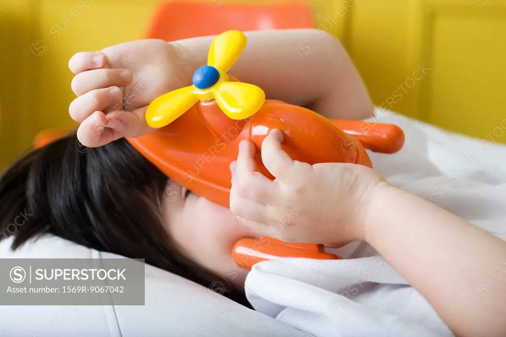 Little boy covering face with toy helicopter