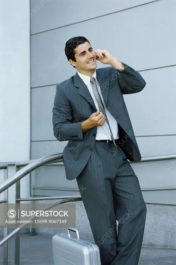 Businessman using cell phone, leaning against railing