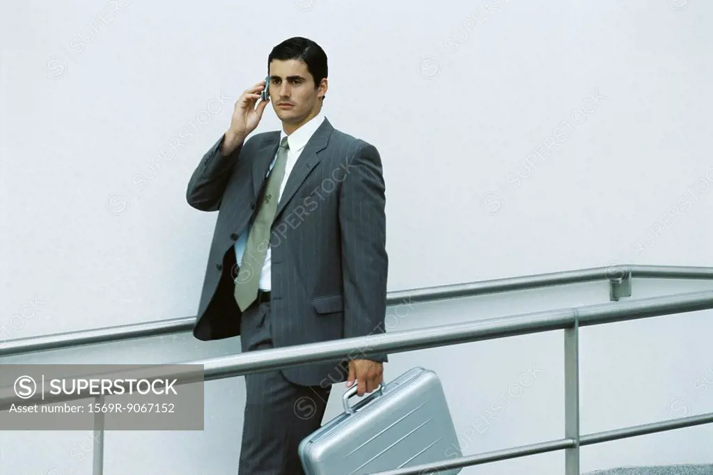 Businessman walking on sidewalk using cell phone, carrying briefcase