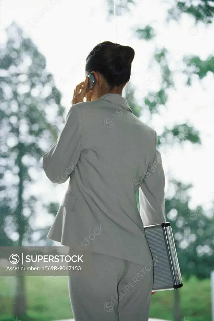 Businesswoman using cell phone, carrying briefcase under arm, rear view