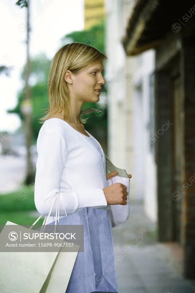 Woman carrying shopping bags on arm window shopping, side view