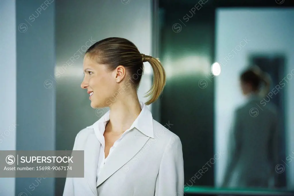 Businesswoman emerging from elevator, looking away smiling