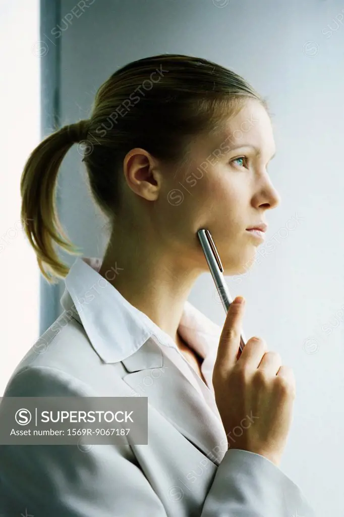 Young businesswoman looking away in thought, holding pen up to face