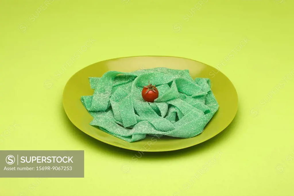 Food concept, plate of green gummy candy arranged like pasta topped with cherry tomato