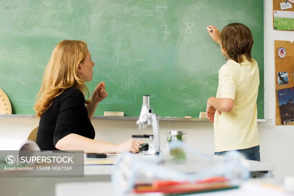 Teacher watching boy writing on blackboard
