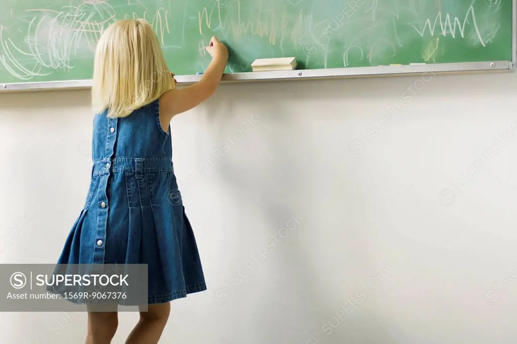 Little girl scribbling with chalk on blackboard