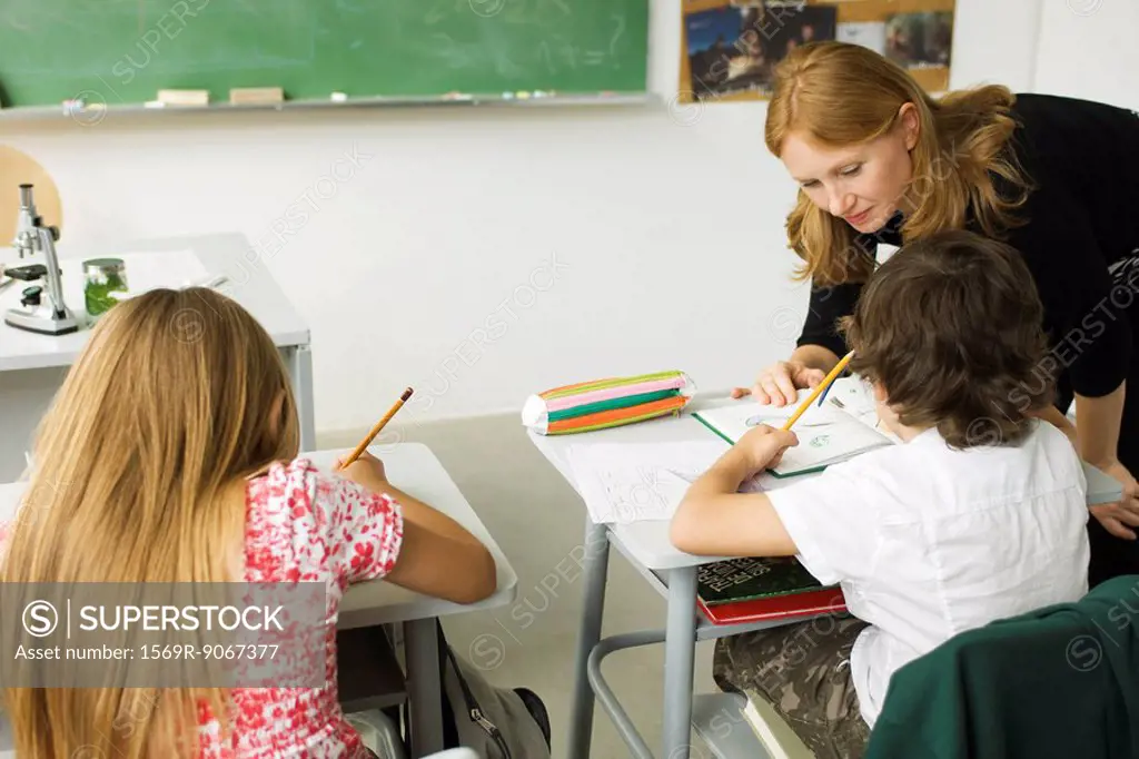 Elementary teacher leaning over student´s desk, helping him with assignment