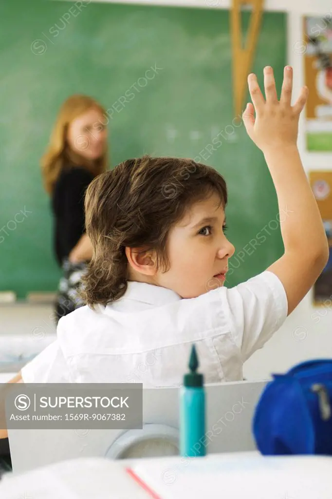 Boy raising hand in class, looking over shoulder
