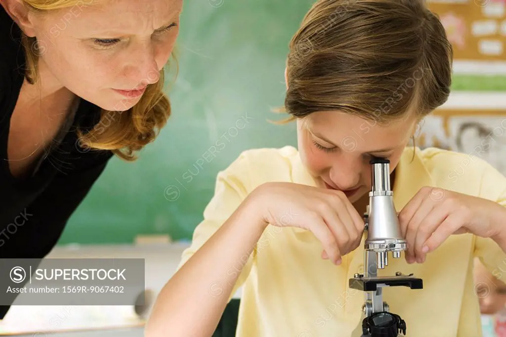 Elementary teacher watching student using microscope