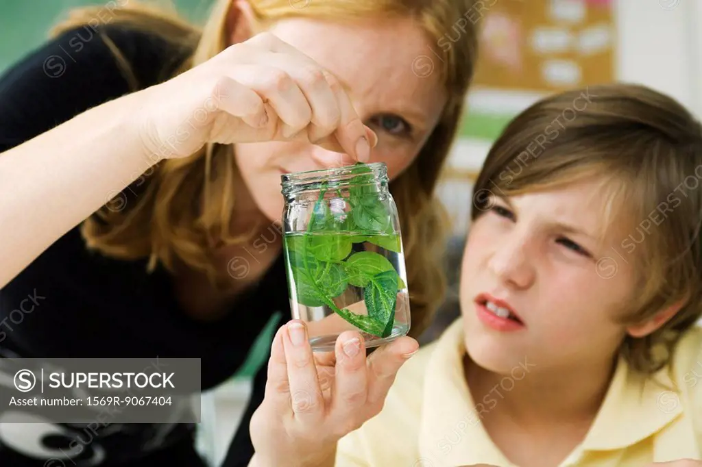 Elementary teacher showing student plant specimen in jar