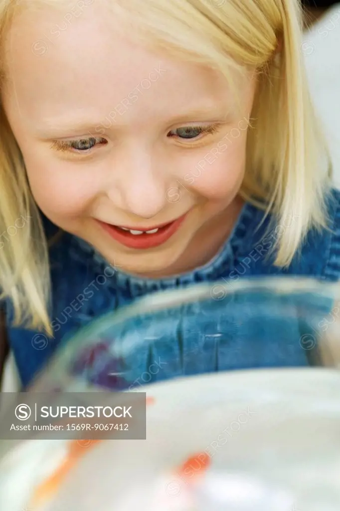 Little girl looking at goldfish in bowl, high angle view