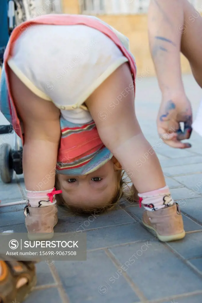 Toddler girl bending over, peeking through legs at camera