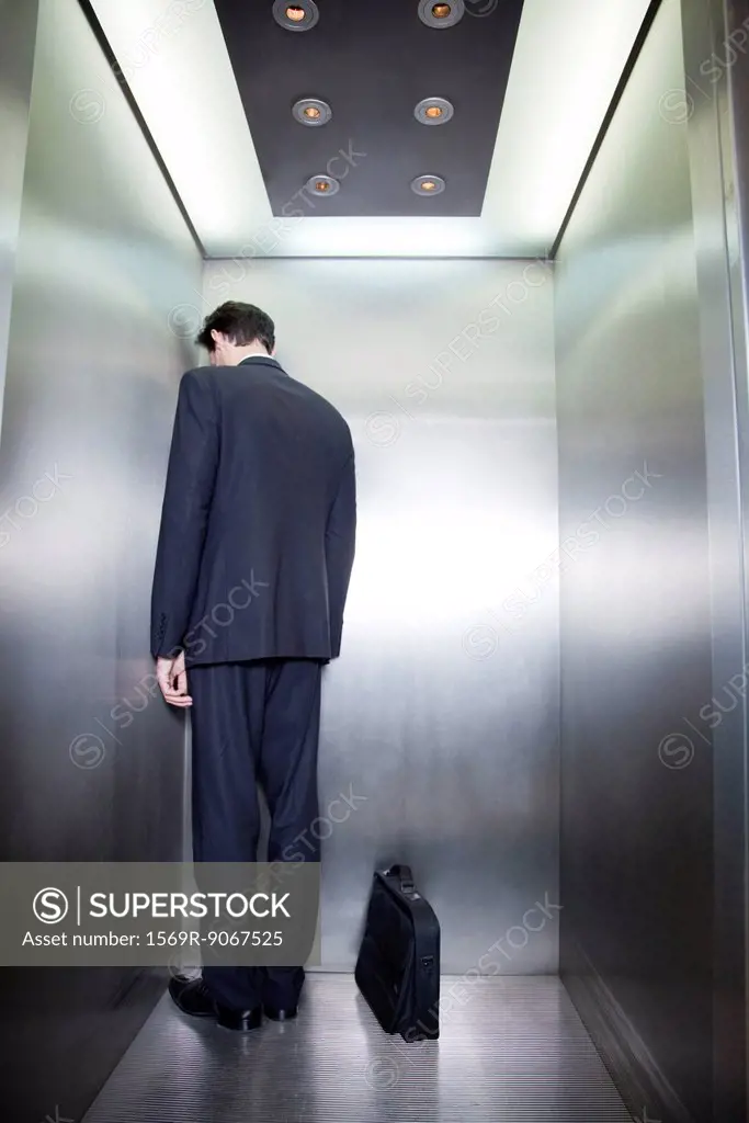 Businessman standing in corner of elevator with back to camera and head down