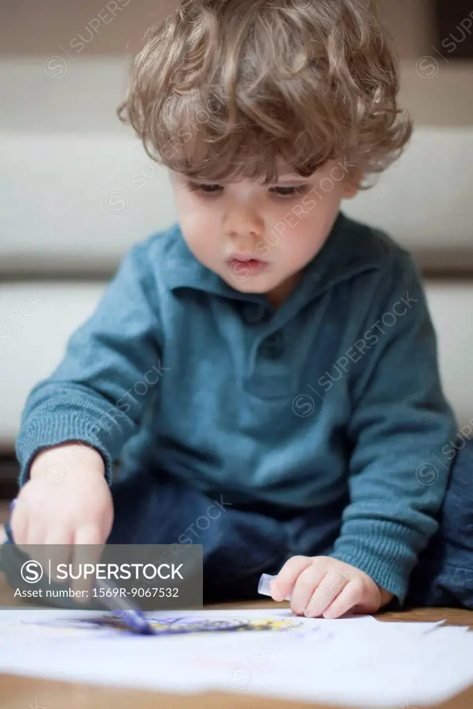 Toddler boy sitting on floor, drawing on paper