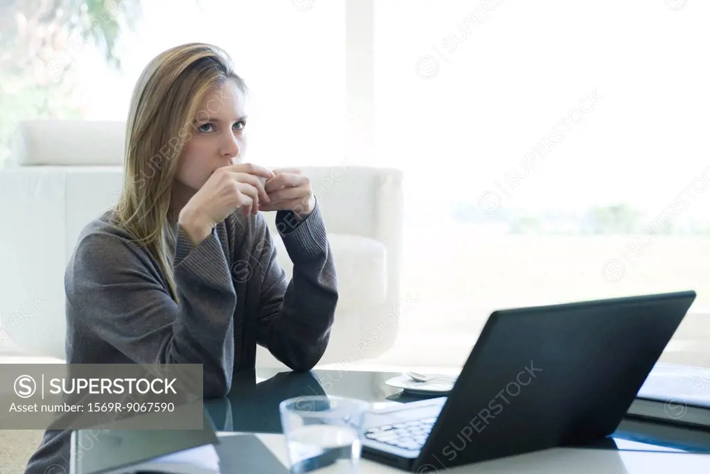 Woman sitting at coffee table with laptop computer, drinking coffee