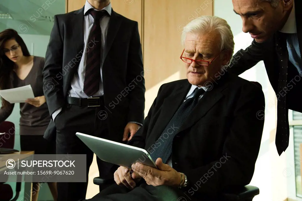 Executives looking down at digital tablet and having discussion