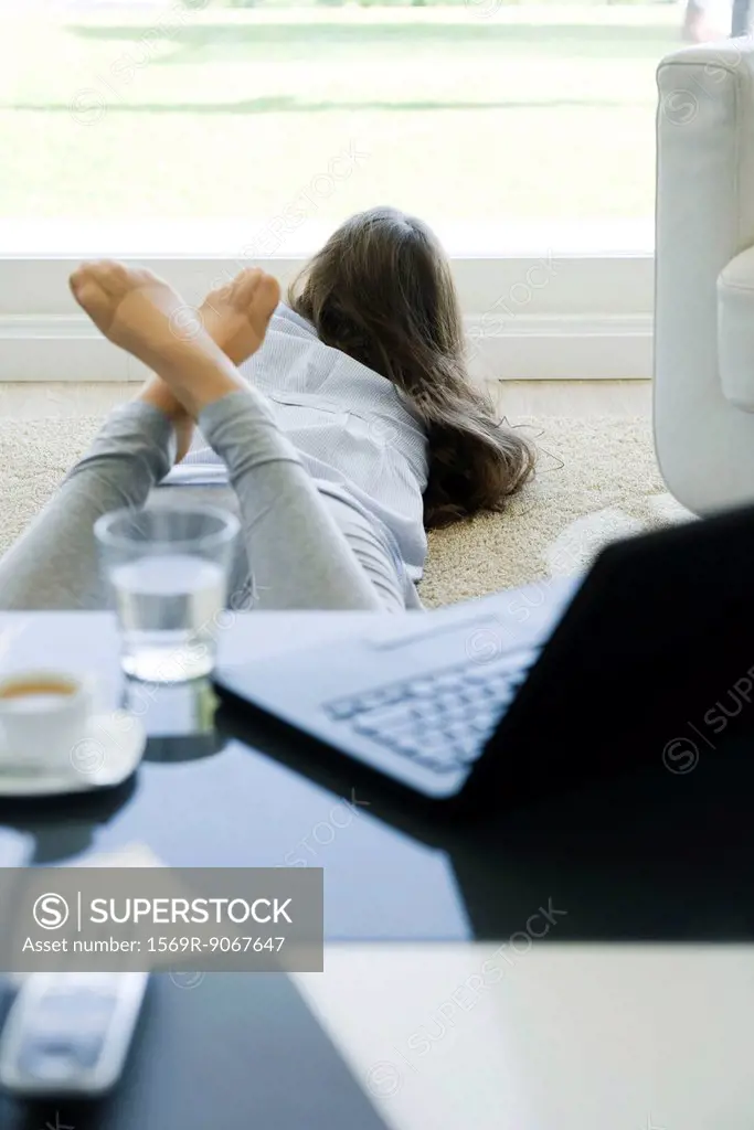 Young woman lying on stomach on floor, looking out window