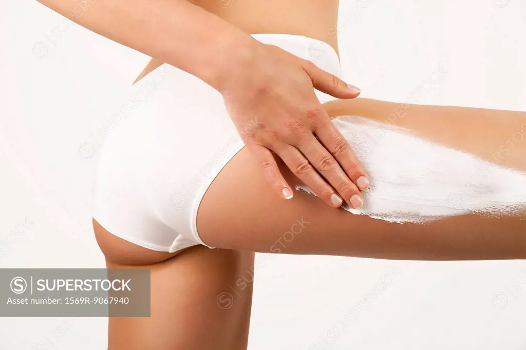 Woman applying moisturizer to thigh, cropped