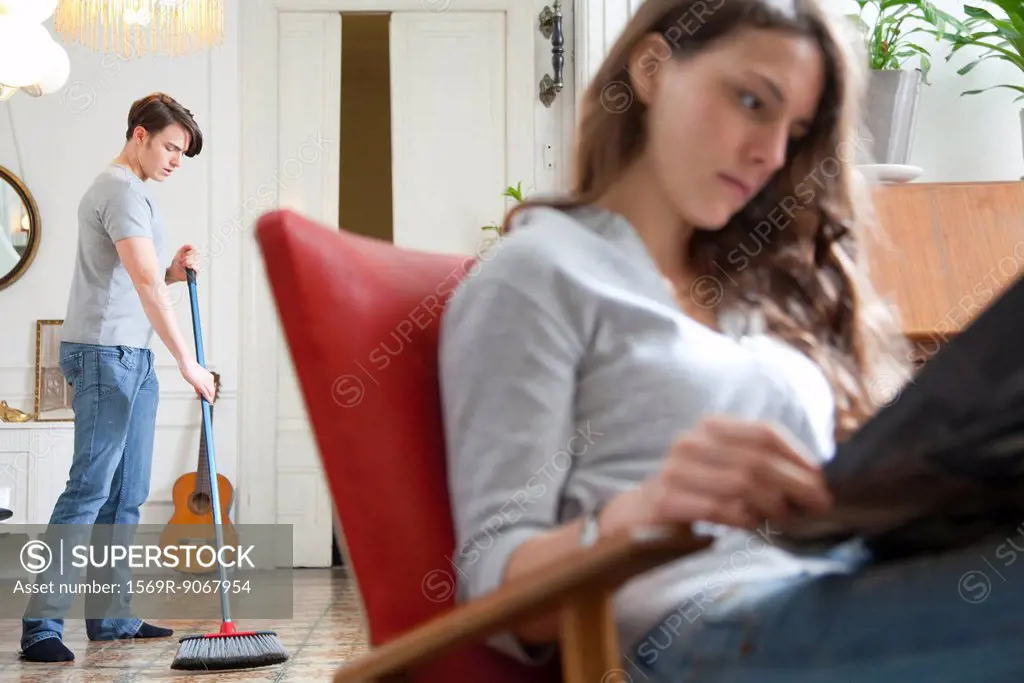 Man sweeping floor while wife reads
