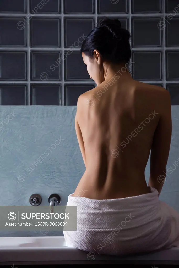 Woman sitting on edge of bathtub, rear view