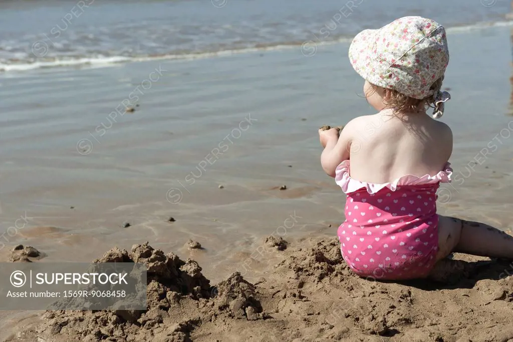 Toddler girl playing in sand at the beach, rear view