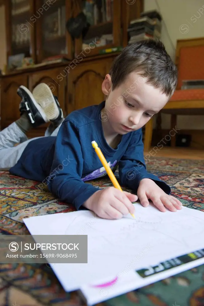 Boy lying on floor, drawing on paper with pencil