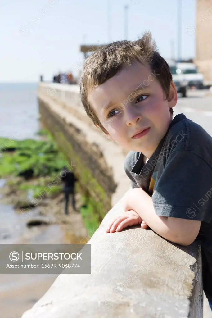 Boy leaning against waterfront railing, looking at view