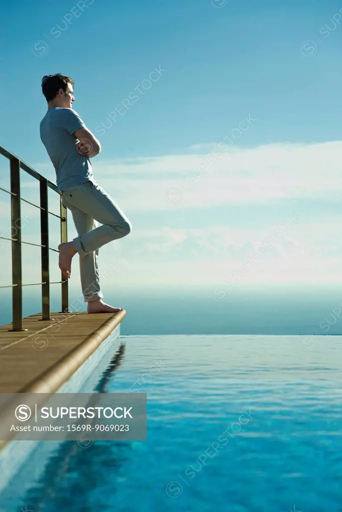 Man leaning against railing beside infinity pool, looking at view