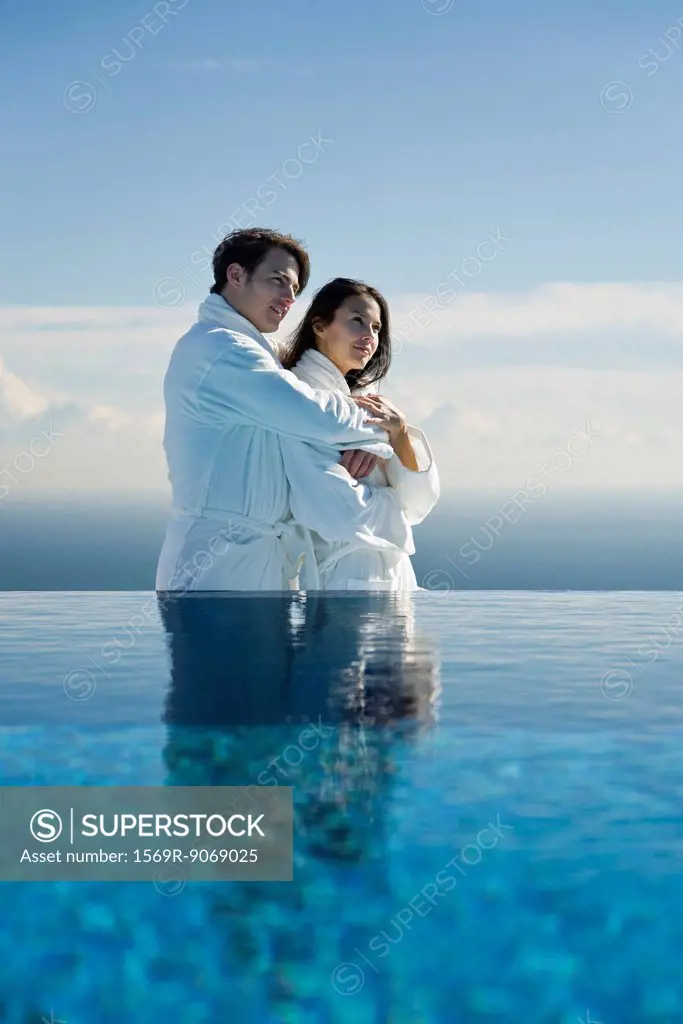 Couple embracing at edge of infinity pool, both wearing bathrobes