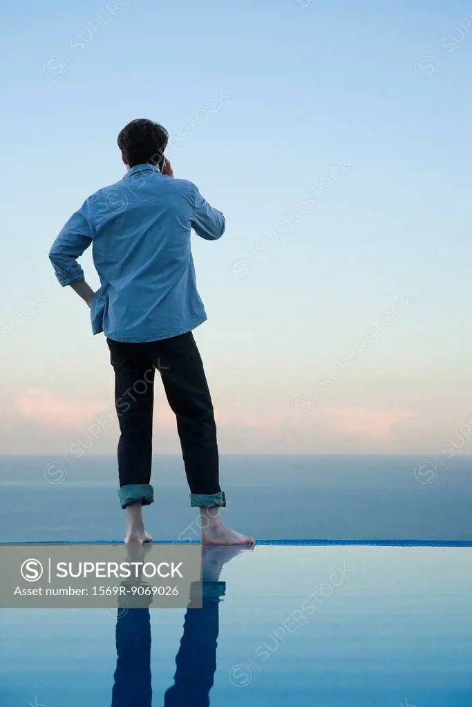 Man standing on edge of infinity pool, talking on cell phone