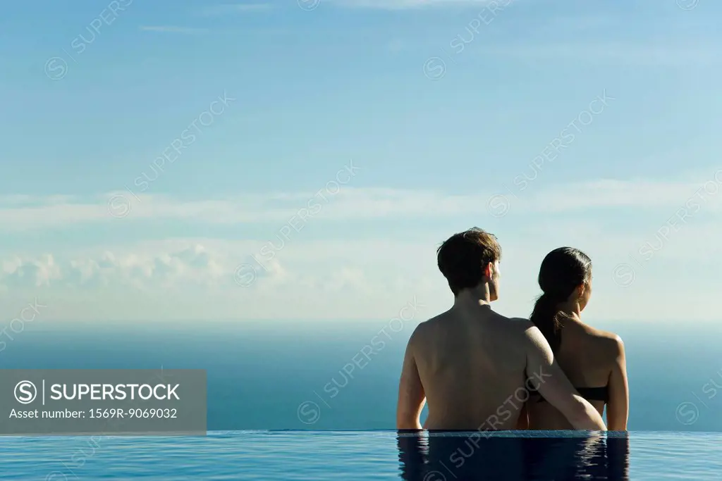 Couple standing at edge of infinity pool, looking at view