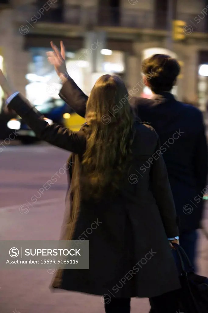 Couple hailing taxi at night, rear view