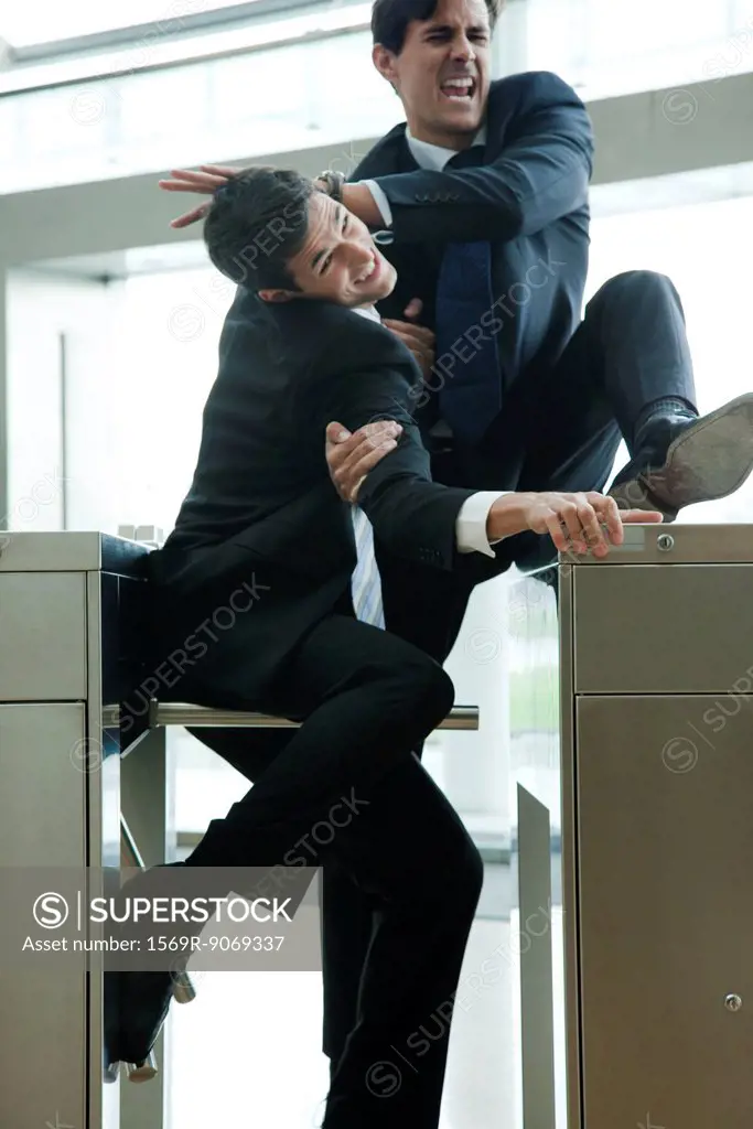 Businessmen fighting to beat each other through turnstile