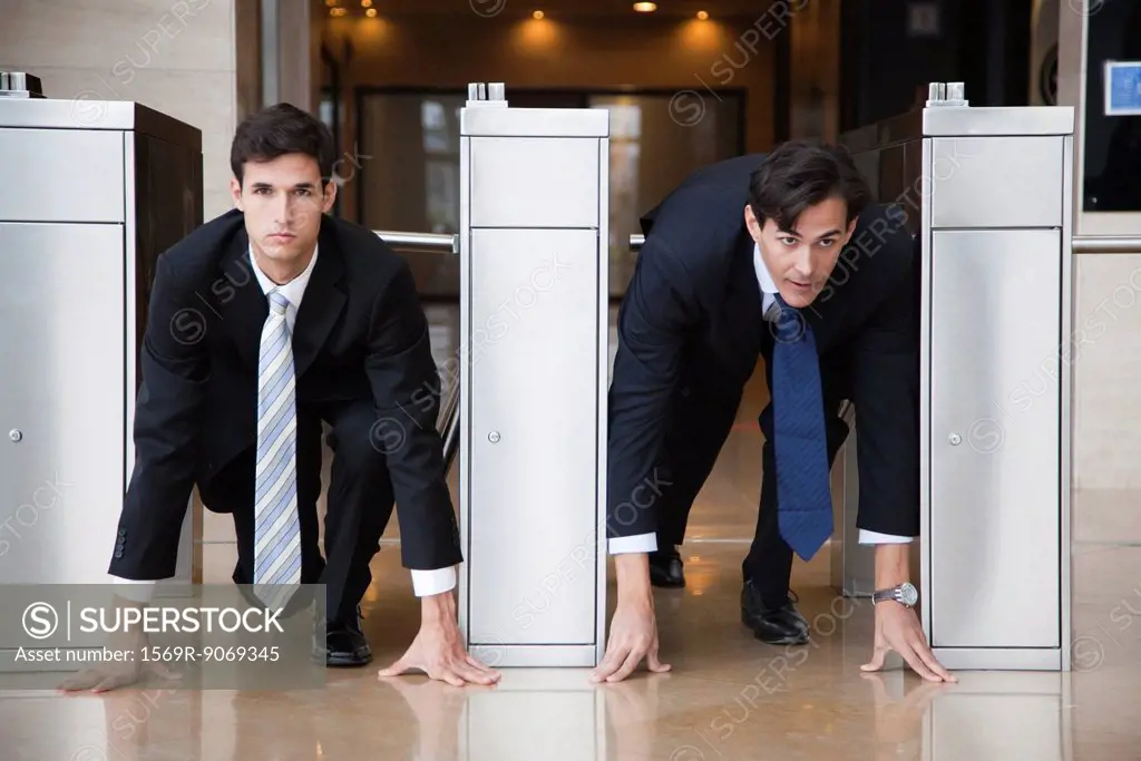 Businessmen crouching in starting position in lobby turnstiles