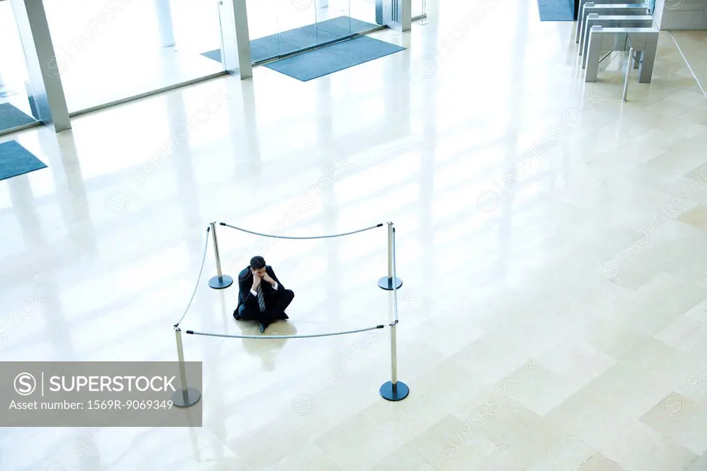 Businessman sitting on floor inside roped off area in lobby