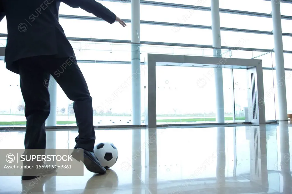 Businessman kicking soccer ball in lobby