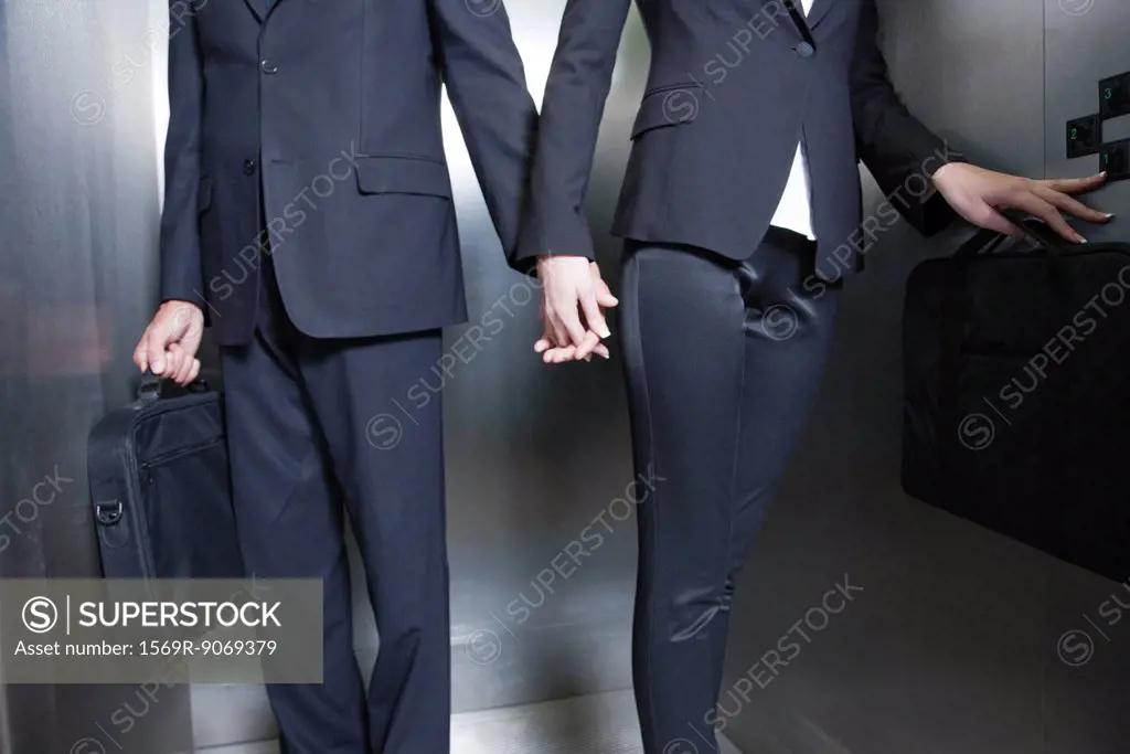 Professionals holding hands in elevator, cropped