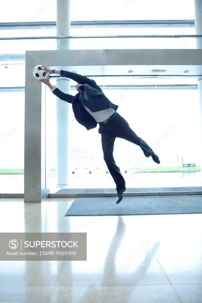 Businessman catching soccer ball in lobby