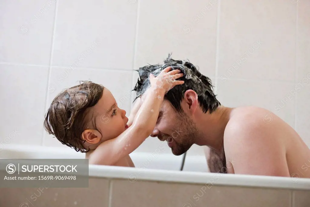 Toddler boy washing father´s hair in bath