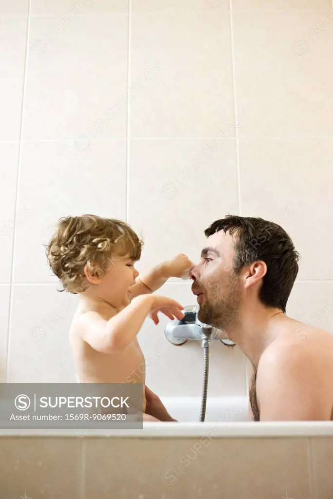 Father and toddler son playing together in the bath